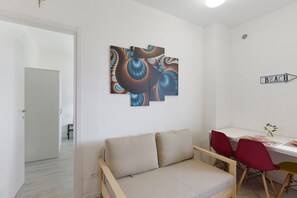 A modern living room with a sofa, a dining table with chairs, and a wall-mounted abstract art piece.