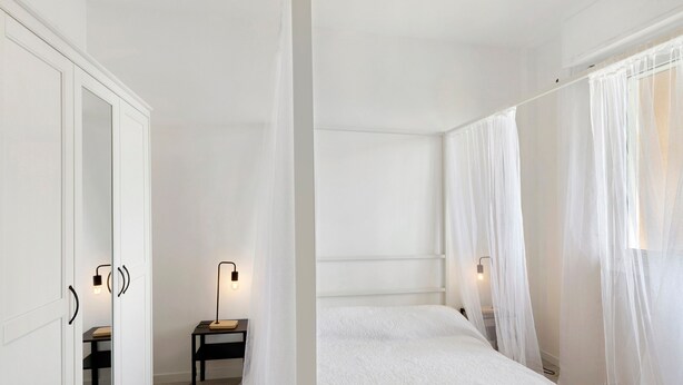 A bedroom with a large bed, a bedside table, a mirror, and sheer curtains. - Vacation Home 'Appartamento A Costarainera' with Sea View, Wi-Fi, and Air Conditioning (Pantai)