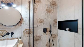 Une salle de bain avec un miroir rond, un lavabo, une douchette à main et une étagère avec des bouteilles.