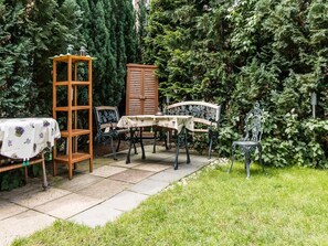 Un patio jardín con una mesa, sillas, un armario de madera y un banco de metal.