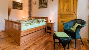 A bedroom with a wooden bed, a nightstand, a wicker chair, and a wooden door. - Apartment 'Romantika 3' with Shared Pool, Shared Garden and Wi-Fi (Potsdam)