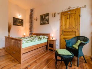 Une chambre avec un lit en bois, une table de chevet, une chaise en osier et une porte en bois.