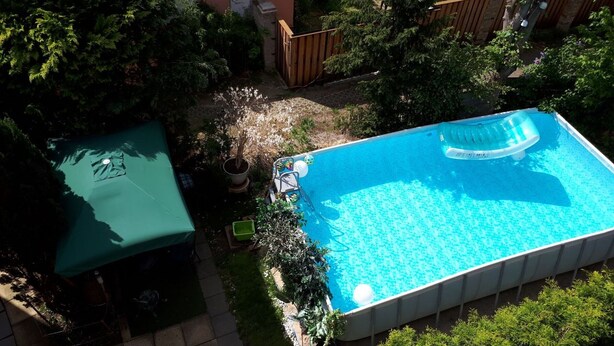 A rectangular swimming pool with a floating seat, surrounded by a wooden fence and lush greenery. - Apartment 'Romantika 3' with Shared Pool, Shared Garden and Wi-Fi (Potsdam)