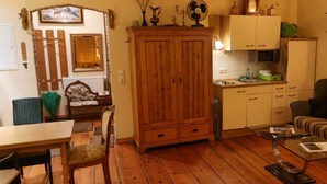 A cozy living room with a wooden cabinet, a striped sofa, and a dining area with a table and chairs. - Apartment 'Romantika 3' with Shared Pool, Shared Garden and Wi-Fi (Potsdam)