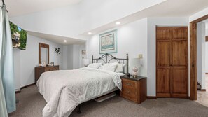 Quarto com cama, mesas de cabeceira, guarda-roupa de madeira, um quadro na parede e espelho.