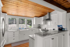 Una cocina moderna con armarios blancos, encimera de mármol y techo de madera.