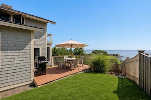 En trädgård med en uteplats, utemöbler, en grill och utsikt över havet.