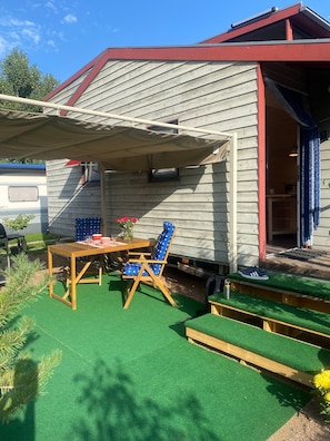 A covered outdoor seating area with a table and chairs, a small table with a vase of flowers, and a bench. - Tiny Home “Tinyhaus Adelheid am Silbersee” (Freiburg im Breisgau)