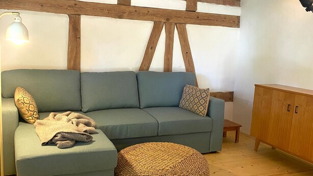 A cozy living room with a sectional sofa, a round ottoman, a small wooden table, and a cabinet.