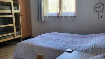 A bedroom with two beds, a wooden wardrobe, a window with curtains, and a dreamcatcher on the wall.