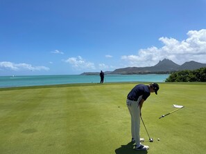 Een golfbaan met vrij uitzicht op de oceaan en bergen op de achtergrond.