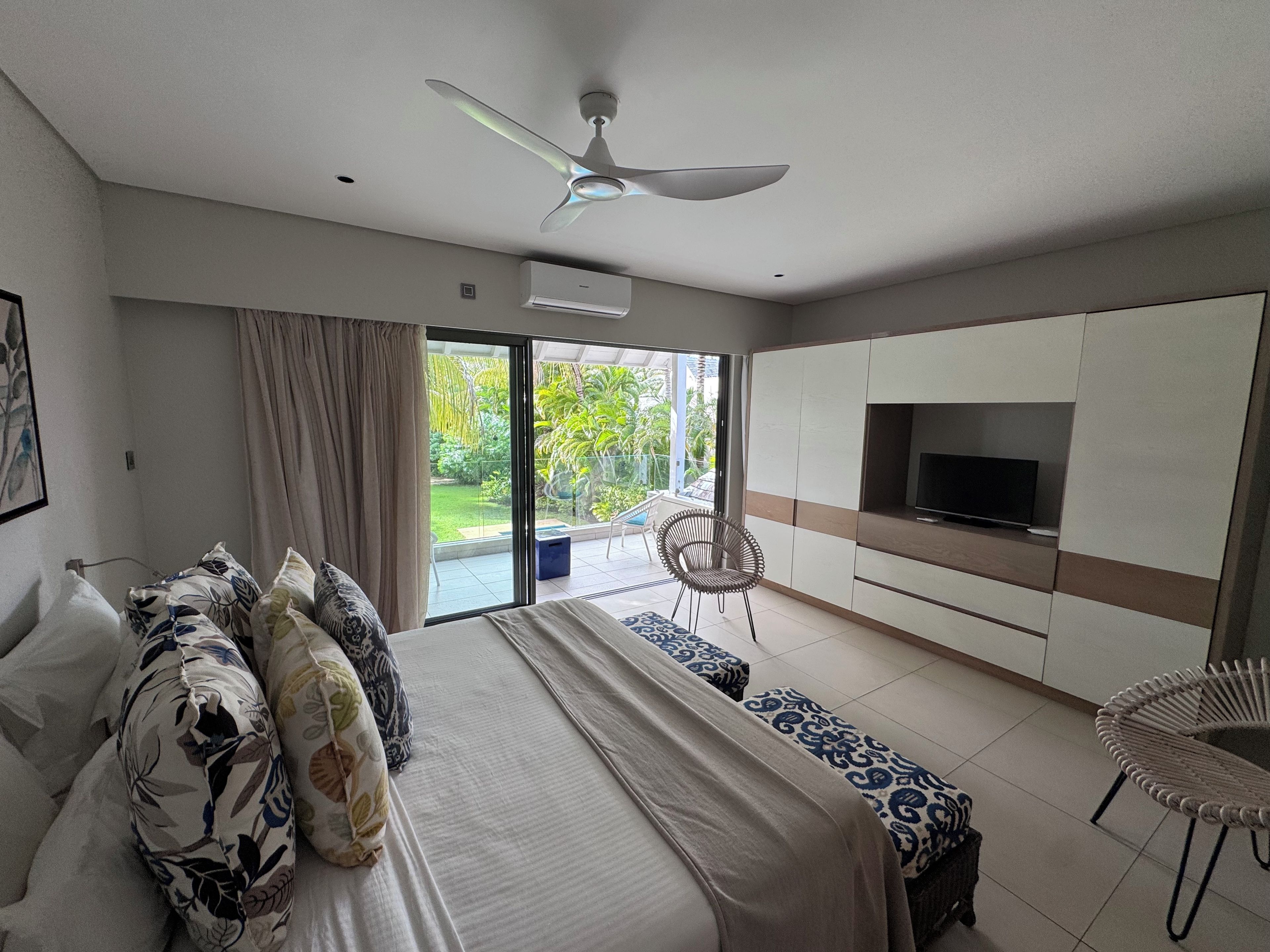 Een slaapkamer met een bed, een televisie, een plafondventilator en een schuifdeur naar een balkon.