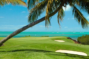 Un parcours de golf offrant une vue dégagée sur l’océan et les bateaux au loin.