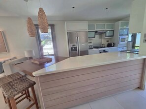 Een moderne keuken met een centraal eiland, ingebouwde apparatuur en een eethoek met een tafel en stoelen.
