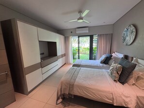 A bedroom with a bed, a TV, a ceiling fan, and a view of greenery outside. - "VILLA PLENITUDE ANAHITA" | Private pool, golf course view, access to the resort (Beau Champ)