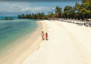 Een strand met helder turquoise water, een zandstrand en een rij rieten parasols.