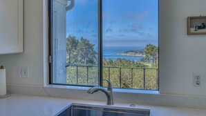 A kitchen with a large window overlooking a scenic view of trees and the ocean.
