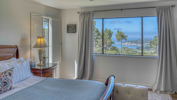 A bedroom with a bed, a nightstand, a lamp, a ceiling fan, and a large window with curtains.