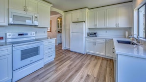 A modern kitchen with white cabinetry, a built-in microwave, a stainless steel oven, and a refrigerator.