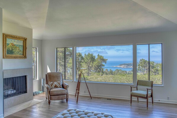 A spacious room with a large window overlooking a coastal landscape, a fireplace, and a comfortable seating area.