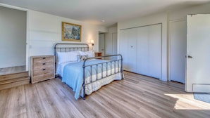 A bedroom with a metal bed frame, a nightstand, a wooden dresser, and a door. - Pebble Beach Escape - Golf, Ocean & Sunset Views (Pebble Beach)