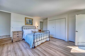 A bedroom with a metal bed frame, a nightstand, a wooden dresser, and a door.