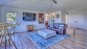 A spacious living room with a ceiling fan, a mounted television, a leather sofa, a dining area with a glass table, and a patterned rug.