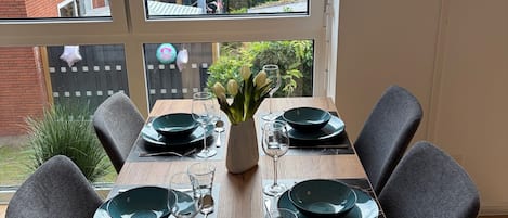 A dining table set for four with a view of a garden and neighboring houses.