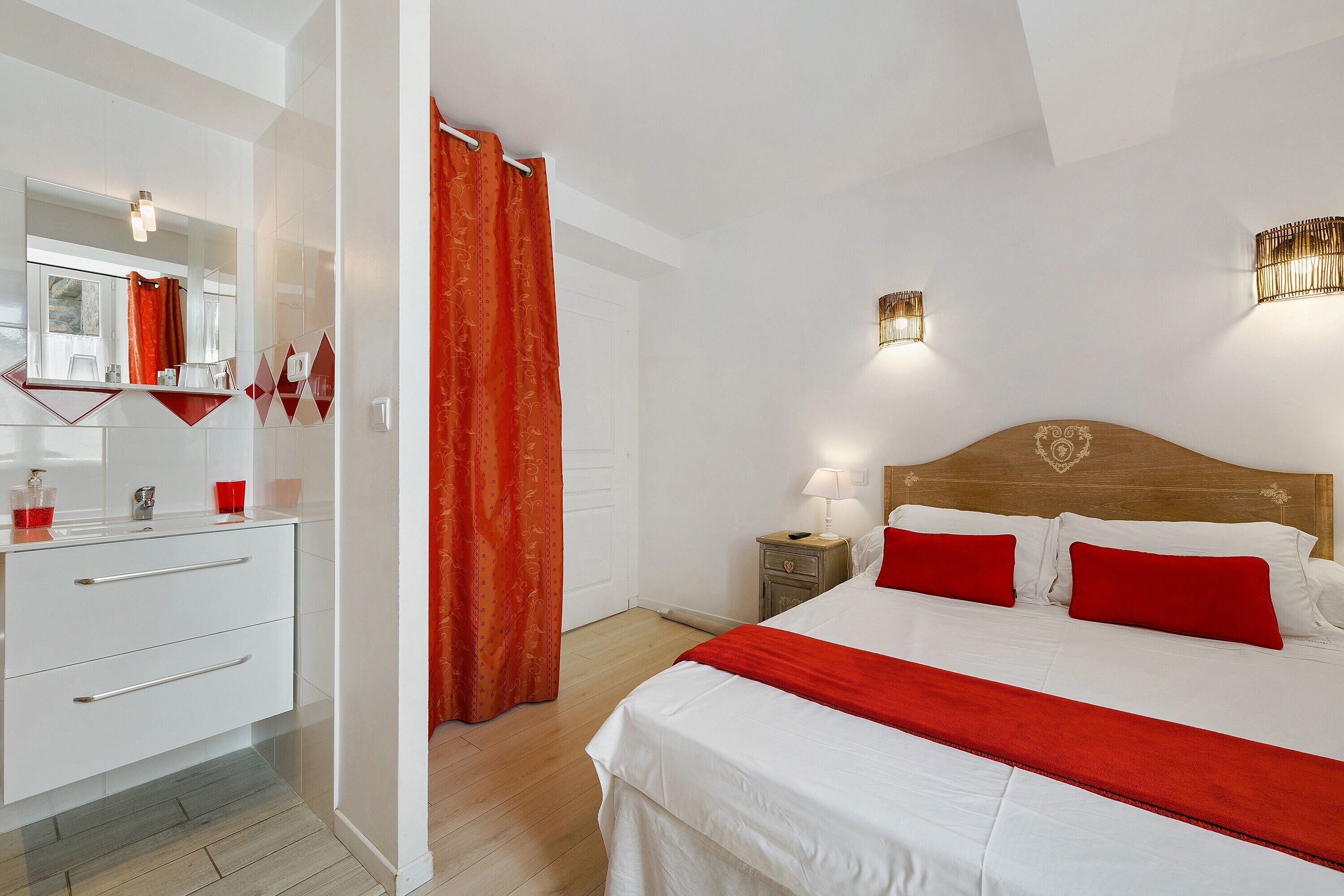 Una camera d'albergo con un letto, un comodino, uno specchio e un bagno con tenda da doccia.