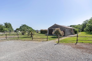 A gravel path leading to a rustic building with a sloped roof, surrounded by a wooden fence and greenery.
