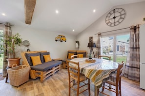A cozy living area with a sofa, dining table, and chairs, a wooden floor, and a large window with curtains.