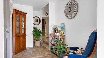 A hallway with a wooden cabinet, a large wall clock, a blue chair, and a bookshelf with books and decorative items.