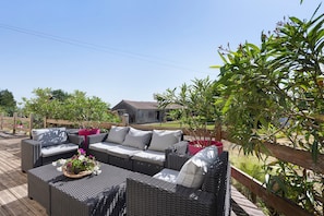 An outdoor patio with wicker furniture, a wooden deck, and a house in the background.