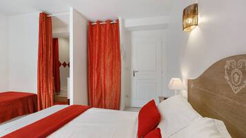 A hotel room with a bed, a nightstand, a lamp, a door, and red curtains.