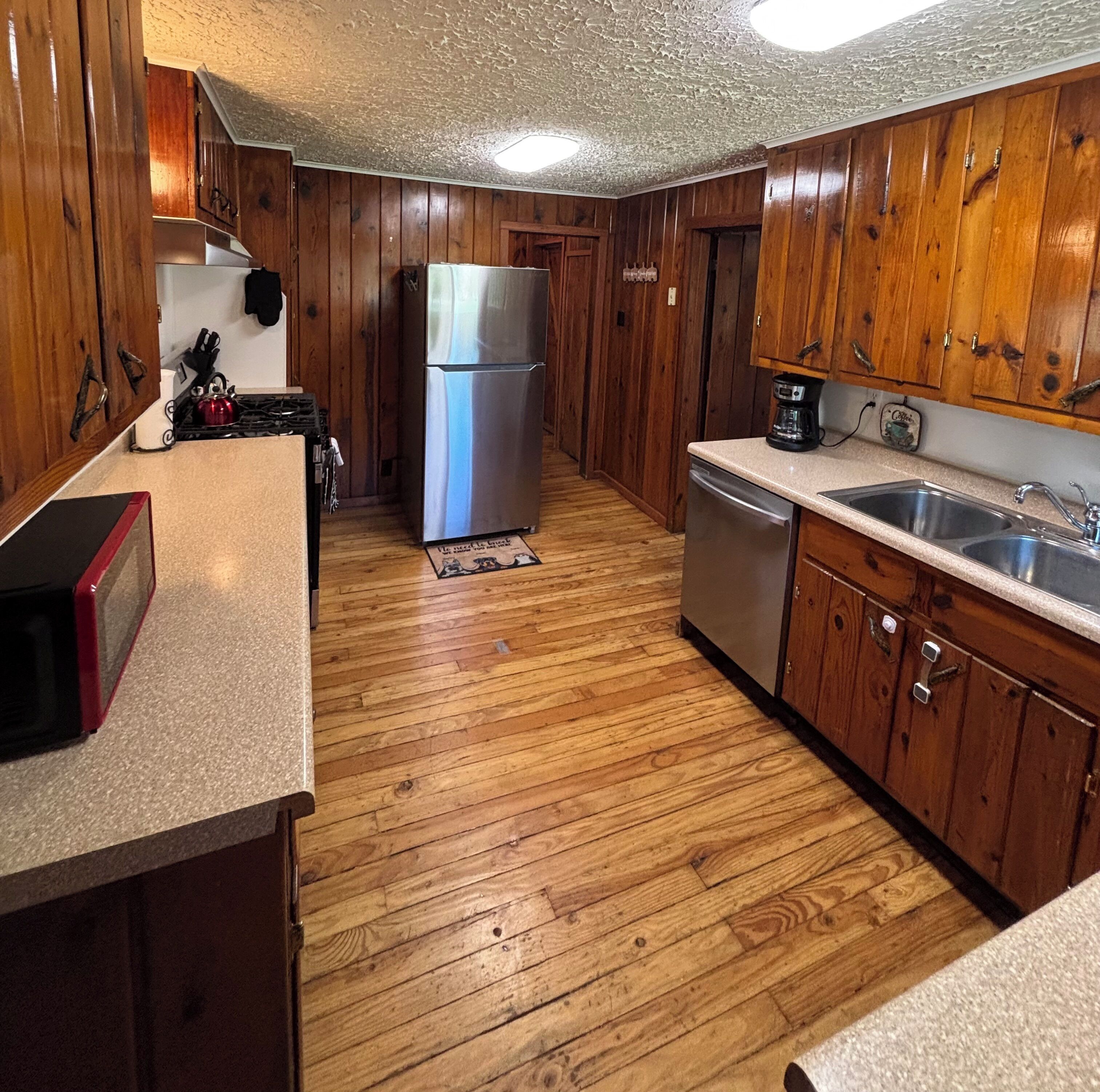 Una cocina con armarios de madera, un refrigerador de acero inoxidable, lavavajillas y cafetera.