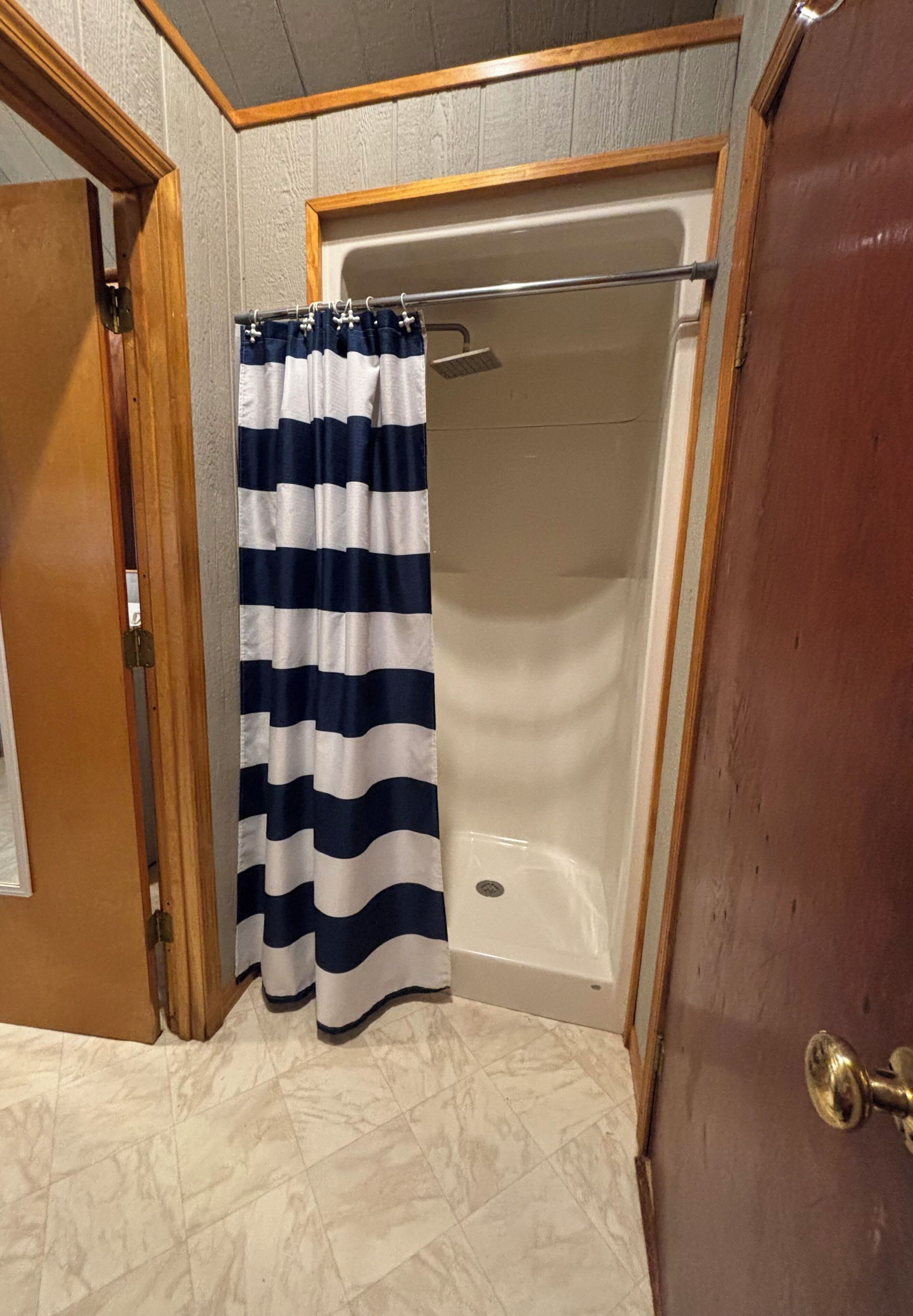 A bathroom with a shower, a striped shower curtain, and a tiled floor.