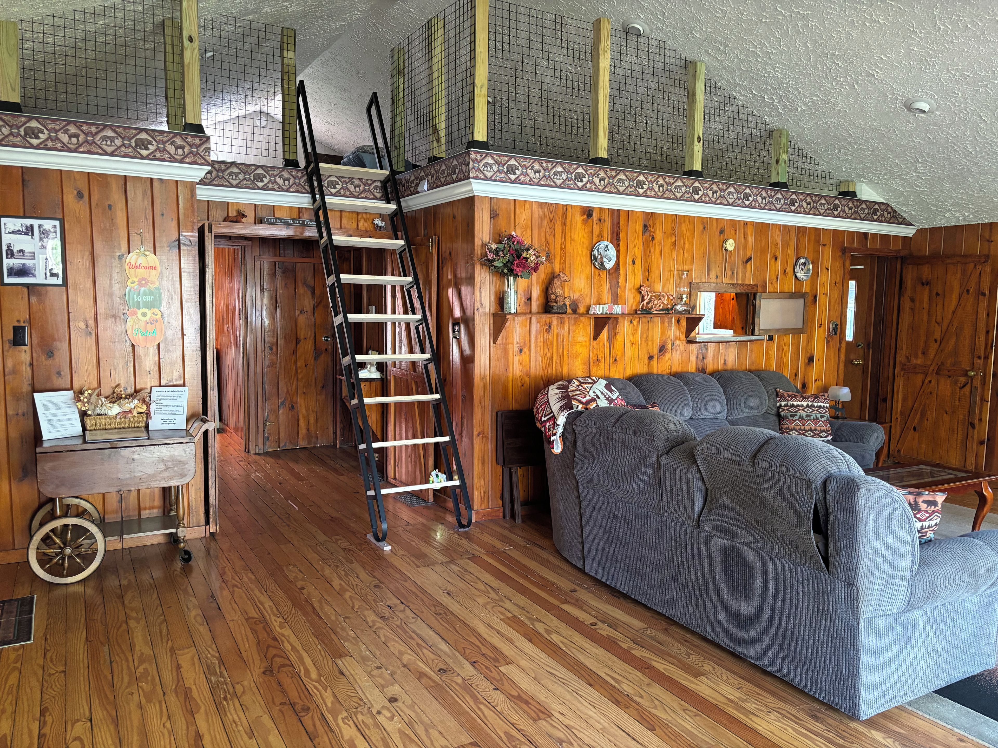 A room with wooden walls, a ladder, a sofa, and a desk with a basket of items.