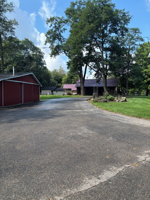 A paved driveway leading to a red barn and a house with a purple roof, surrounded by trees and a grassy area.