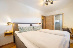 A modern bedroom with a large bed, bedside tables, a wooden wardrobe, and a mirror. - Apartment "Einklang" with Mountain View, Balcony, and Wi-Fi (Krün)