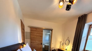 Una camera d'albergo con due letti, una porta in legno, uno specchio, una scrivania e una finestra con tende.