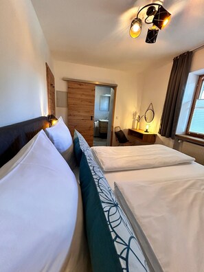 Ein Hotelzimmer mit zwei Betten, einer Holztür, einem Spiegel, einem Schreibtisch und einem Fenster mit Vorhängen.