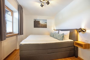 Un dormitorio con una cama grande, una mesita de noche, una lámpara de pared, una ventana con cortinas y un cuadro en la pared.