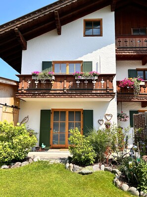 Ein zweistöckiges Gebäude mit einem Balkon, der mit Blumenkästen geschmückt ist, und einer Holztür.