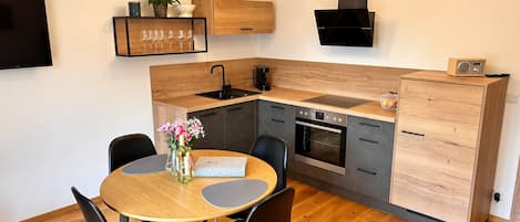 Una cocina moderna con encimera de madera, horno empotrado y comedor con mesa y sillas redondas.