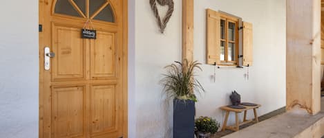 A wooden door with a sign, a potted plant, a small table, and a bench outside a building.