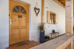 A wooden door with a sign, a potted plant, a small table, and a bench outside a building. - Apartment "Einklang" with Mountain View, Balcony, and Wi-Fi (Krün)