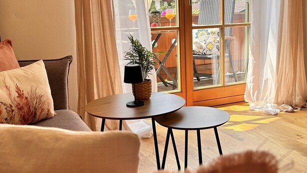 Un accogliente soggiorno con un divano, un tavolino con una pianta e vista su un balcone con mobili da esterno.