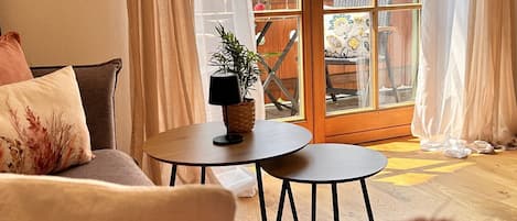 Una sala acogedora con un sofá, una mesita con una planta y vistas a un balcón con mobiliario exterior.