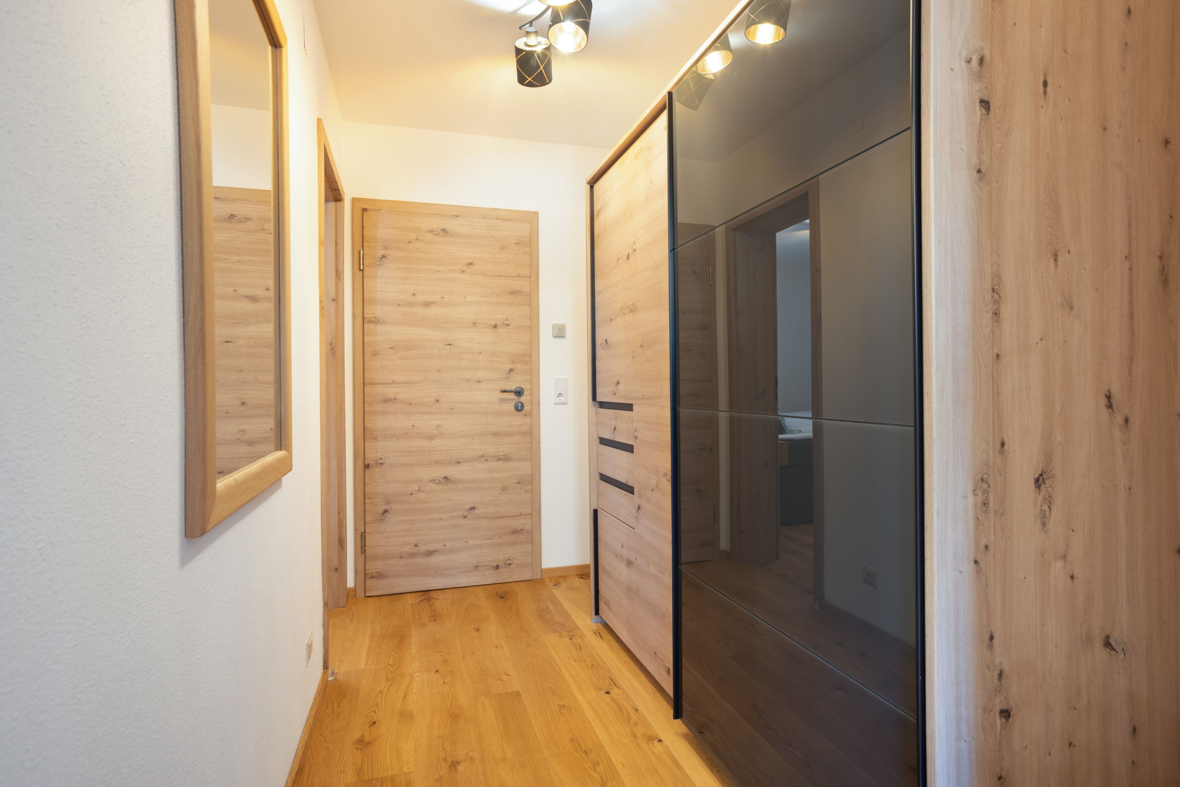 Un couloir doté d’un plancher en bois, d’un mur miroir et d’une porte coulissante donnant sur une pièce.