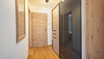 Un pasillo con piso de madera, un muro espejado y una puerta corrediza que da a una habitación.